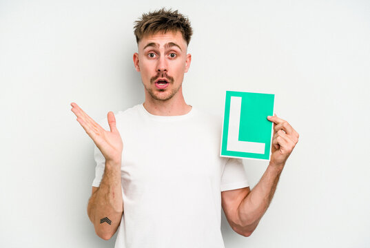 Young caucasian man holding L placard isolated on white background surprised and shocked.