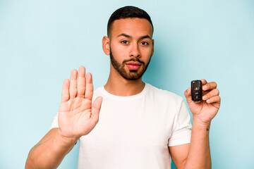 Wall Mural - Young hispanic man holding car keys isolated on blue background standing with outstretched hand showing stop sign, preventing you.