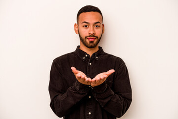 Wall Mural - Young hispanic man isolated on white background holding something with palms, offering to camera.