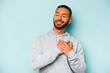 © Asier - Young hispanic man isolated on blue background has friendly expression, pressing palm to chest. Love concept.