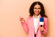 Young African American TV presenter woman isolated on beige background smiling and pointing aside, showing something at blank space.