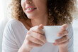 © LIGHTFIELD STUDIOS - partial view of smiling woman with curly hair holding white coffee cup.