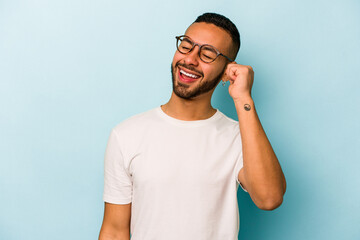 Wall Mural - Young hispanic man isolated on blue background celebrating a victory, passion and enthusiasm, happy expression.