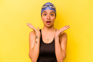 Wall Mural - Young swimmer hispanic woman isolated on yellow background surprised and shocked.