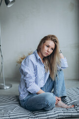 Wall Mural - Young girl in casual relaxed pose at home. Young blonde emotional sensual woman in jeans