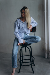 Wall Mural - Young girl in casual relaxed pose at home. Young blonde emotional sensual woman in jeans