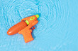 Water gun toy on blue water surface with rippled waves. Fun, leisure summertime background. Copy space