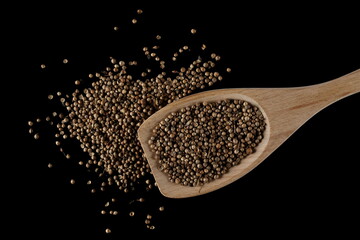 Coriander seeds with wooden spoon isolated on black background, top view