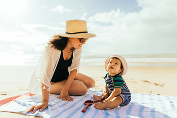 Wall Mural - Mother and her baby son playing on the beach during summer vacation