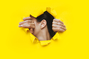 Wall Mural - Female ear and two hands close-up. Copy space. Torn paper, yellow background. The concept of eavesdropping, espionage, gossip and the yellow press.