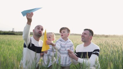 Wall Mural - Gay male couple having fun with sons children outdoor - LGBTQ family playing with airplane paper toy