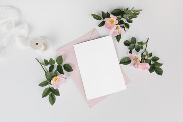 Wall Mural - Summer wedding stationery mock-up scene with silk ribbon. Blank greeting card, invitation, pink envelope and blooming dog rose flowers isolated on white table background. Flat lay, top view.