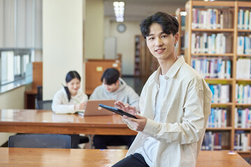 아시아 한국의 대학교 도서관에서 2명의 남녀 모델 배경으로 책상위에 앉아서 테블릿을 보는 젊은 대학생 남자 모델