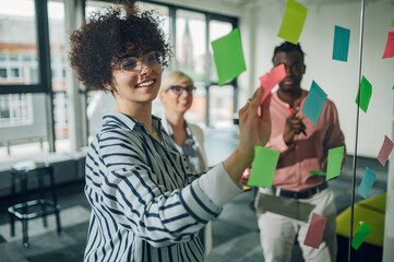 Multiracial team at work writing ideas on sticky notes on the glass wall