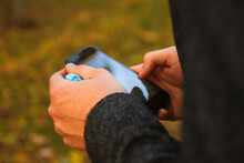 Defocus Male Hand Holding Phone. Man Using Smart Phone In Autumn Park. Typing Text Message Or Reading Social Media At Mobile Phone. Fall Background. Cell Phone. Communication. Nature. Out Of Focus