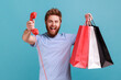 © khosrork - Portrait of excited positive bearded man holding shopping bag and red retro telephone, call me, looking at camera with excitement. Indoor studio shot isolated on blue background.