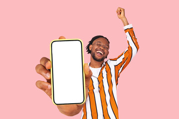 Yes. excited happy celebrating positive bearded a man in striped shirt showing screen on his smartphone mobile cellphone and rejoicing. Indoor studio shot isolated on pink background.