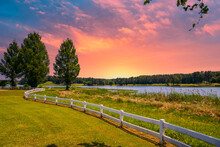 A Gorgeous Summer Landscape At Lake Acworth With Rippling Blue Lake Water Surrounded By Lush Green Grass And Trees With A White Wooden Fence And Powerful Clouds At Sunset At Cauble Park
