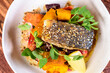 A serving of grilled barramundi fish with roast vegetables in a round white bowl