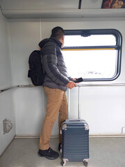 Latino adult man is transported on the light rail without a driver arriving in Vancouver Canada with a face mask due to the Covid-19 pandemic, he uses his cell phone to see maps and send messages
