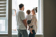 © Galina Zhigalova - Young family man father and mother woman with baby girl on window sill looking at window at home