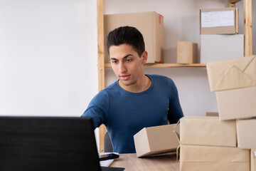 Muslim male business owner sitting at home office. using computer, online marketing packaging box delivery, SME e-commerce telemarketing