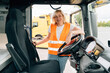 © troyanphoto - Mature woman truck driver steering wheel inside lorry cabin. Happy middle age female trucker portrait
