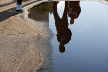 Defocused View To People Reflection In Puddle On A Street. Rain In Summer City, Wet Asphalt