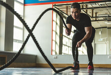 Portrait Shot Of Strong Young Man Training With Battle Ropes In The Exercise Gym