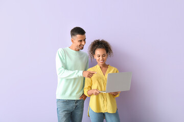 Wall Mural - Young couple using laptop on lilac background