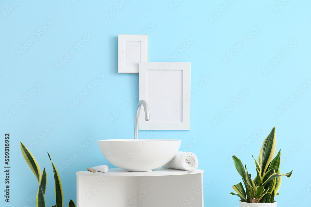 Table with sink, towel and blank frames on blue wall