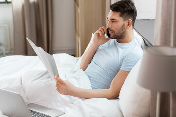 Sticker - people, technology and remote job concept - man with folder and laptop computer calling on smartphone in bed at home bedroom