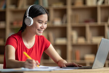 Cheerful Teen Korean Female In Headphones Listen Lesson At Laptop In Room Interior, Profile