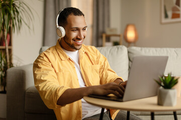 Poster - Young African American man in headphones working online, using laptop at home office, copy space