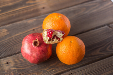 A red fresh pomegranate and two orange on a wooden table