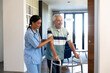 © wavebreak3 - Biracial female physiotherapist assisting happy caucasian senior man in walking with walker at home