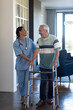 © WavebreakMediaMicro - Biracial female physiotherapist talking and assisting caucasian senior man in walking with walker