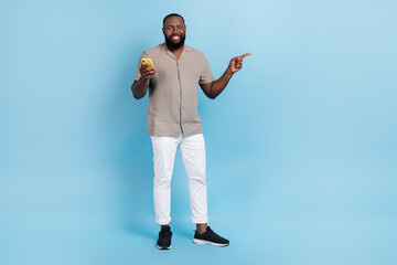 Wall Mural - Full length portrait of handsome cheerful guy hold telephone indicate finger empty space blank isolated on blue color background