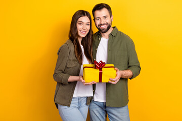 Poster - Portrait of two cheerful peaceful people hold giftbox look camera isolated on yellow color background