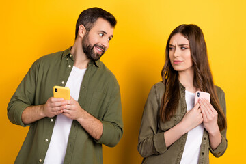 Wall Mural - Photo of cheerful funny husband asking wife about sms notifications she hide isolated on yellow color background