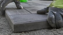 builder's hands laying concrete square paving slabs on sand and pounding with heavy rubber mallet for compaction and leveling. Pavement paving with patterned paving stones