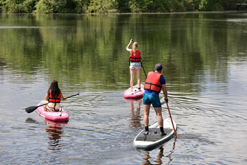 Sup surfing, man and two girls with paddles sailing on a boards in river. Stand up paddle boarding in summer