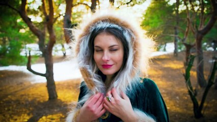 Wall Mural - Portrait happy fantasy woman looks at camera, smiling face. Princess cute girl. Green long warm medieval clothing cape dress hood on head with fur. Nature green pine tree snow sun light winter forest