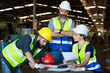 © atitaph - Male and female engineers chat with factory workers as they use machine drawings, planning for industrial maintenance