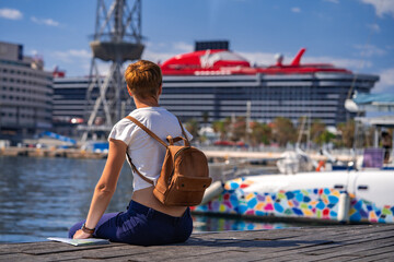 Woman traveler in the Port Vell  with large Virgin cruise liner on the background. Barcelona, Spain - May 29, 2022