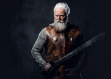 Studio Shot Of Medieval Elderly Warrior Dressed In Armored Clothes Holding Long Sword.