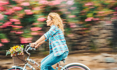 Wall Mural - Happy adult woman ride a bike outdoor with flowers in background. Environment and green transport with bycicle. Cheerful modern female people enjoy active leisure activity riding with a smile