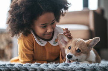 Wall Mural - A curly-haired girl in orange dress playing with a puppy