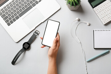 Female hand with mobile phone, wrist watch, earphones and laptop on white background