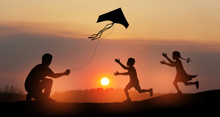 Happy family on the field. Father and kids playing with a kite while running on meadow on the background of the sunset. Funny family time. Happy little children launch a kite with dad.